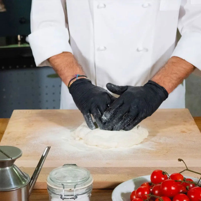 Chef in a kitchen kneading dough on Alfa Beechwood Pastry Board 50x50cm with tomatoes and a jar in the background.