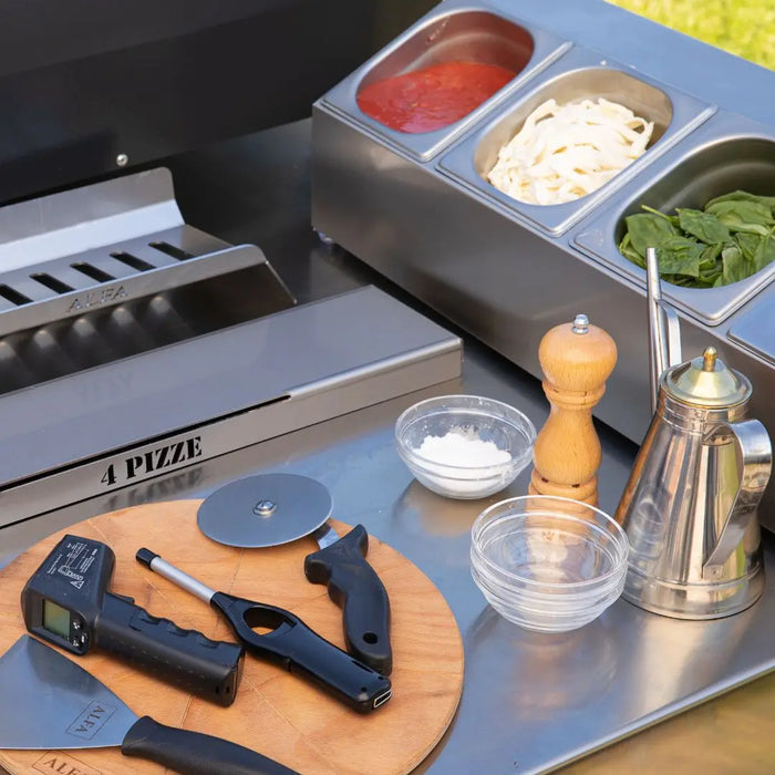 Outdoor Alfa pizza oven topping station with ingredients and tools on a grill