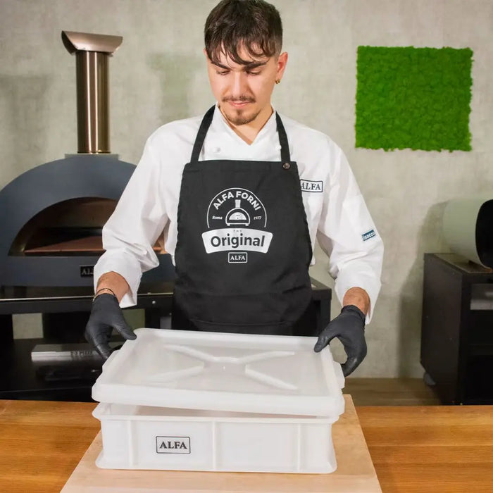 Person wearing an apron with 'Alfa Forni' branding, holding the large white Alfa pizza dough storage box with lid.