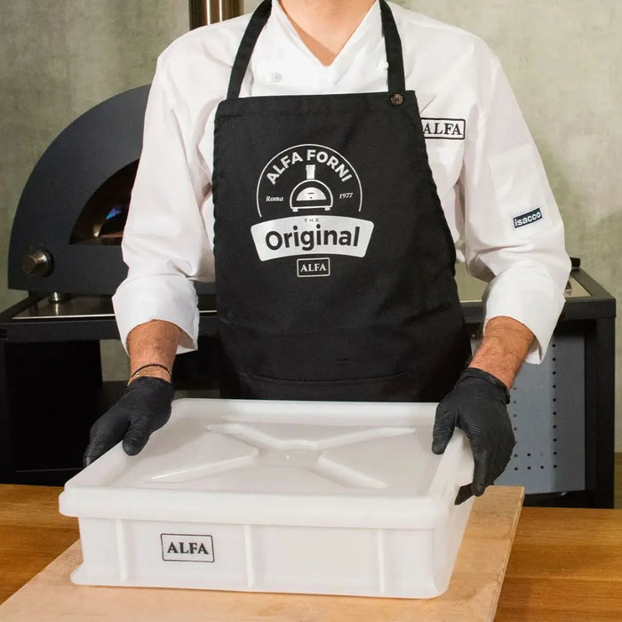 Person wearing an apron with 'Alfa Forni' branding, holding the large white Alfa pizza dough storage box with lid.