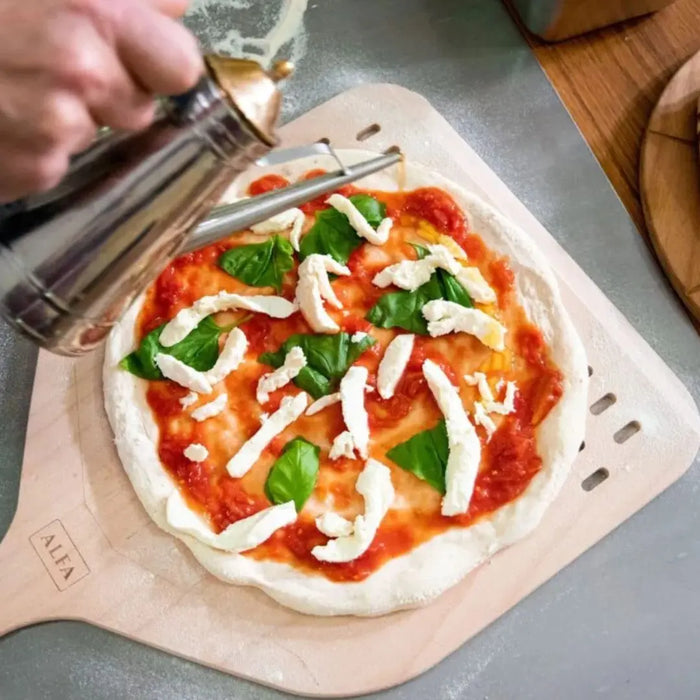 Person seasoning a pizza with herbs on a Alfa wooden pizza peel