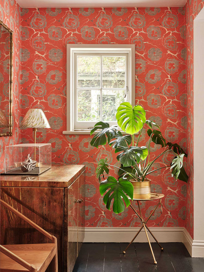 Room interior with red floral wallpaper, metal furniture and a plant.