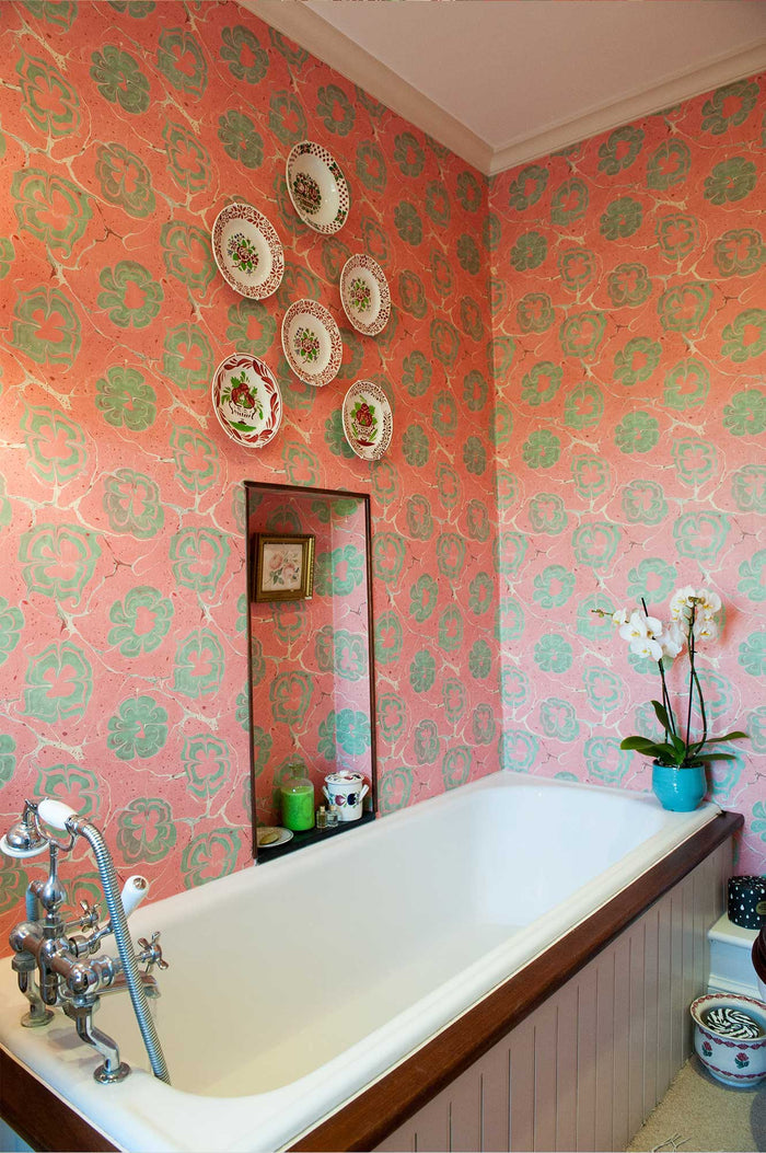 Bathroom with pink floral marbled wallpaper, bathtub and decorative plates.