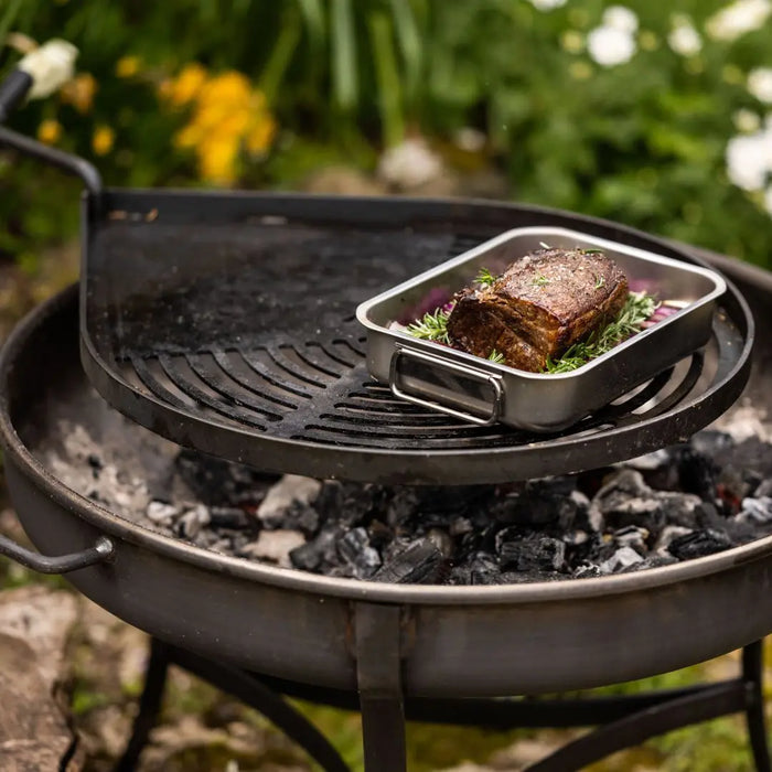 Grilled dish on a pan over charcoal on Dean Forge Moorland Firebowl and Swing Arm Set with a natural outdoor background