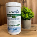 Container of eco3spa water sanitiser tablets on a wooden surface with a plant in the background.
