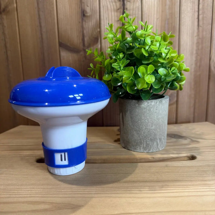 Blue and white hot tub tablet dispenser on a wooden surface with a green plant in the background.