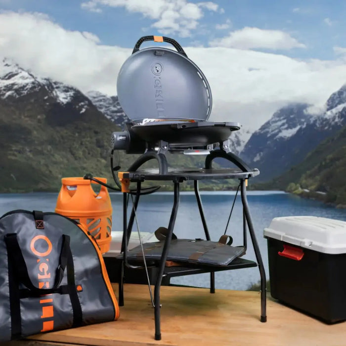 Portable O-Grill on a stand with a scenic mountain and lake background