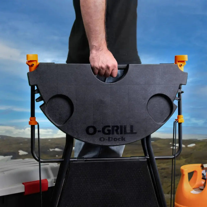 Person holding a black O-Grill with a scenic background