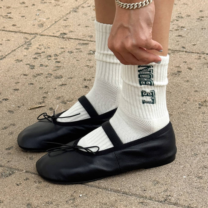 Person wearing black ballet flats and white socks with text, standing on a sidewalk.