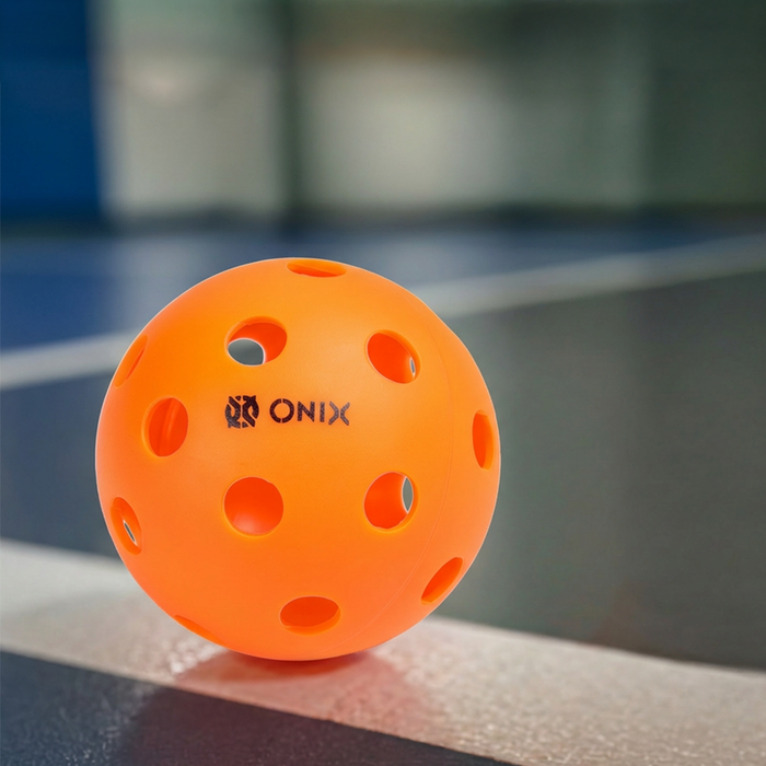 Orange pickleball with Onix branding on a blurred court background