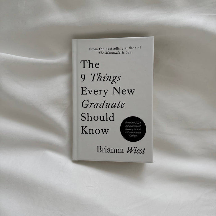 Book titled 'The 9 Things Every New Graduate Should Know' by Brianna Wiest on a white fabric background